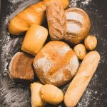 Fresh baked bread with a golden crust, loaf, buns, white, rye on a rustic wooden background with sil rustic. Flat layout close-up.